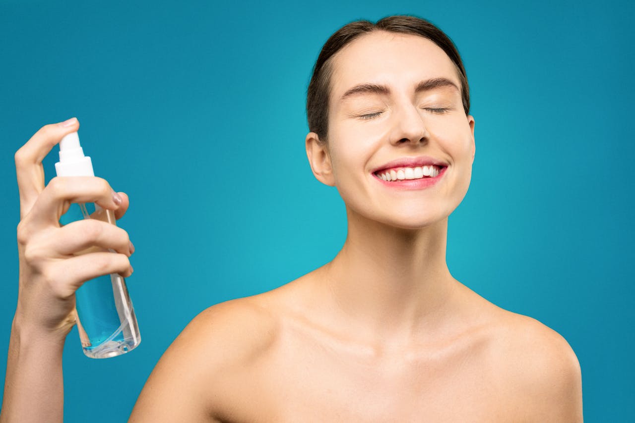 A happy woman with closed eyes sprays facial mist, emphasizing skincare and relaxation.