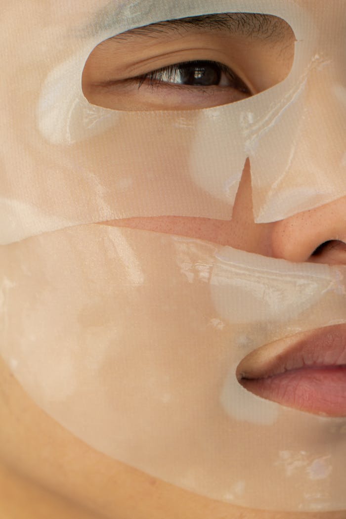 A close-up photo showing the application of a hydrating facial sheet mask on a persons face.